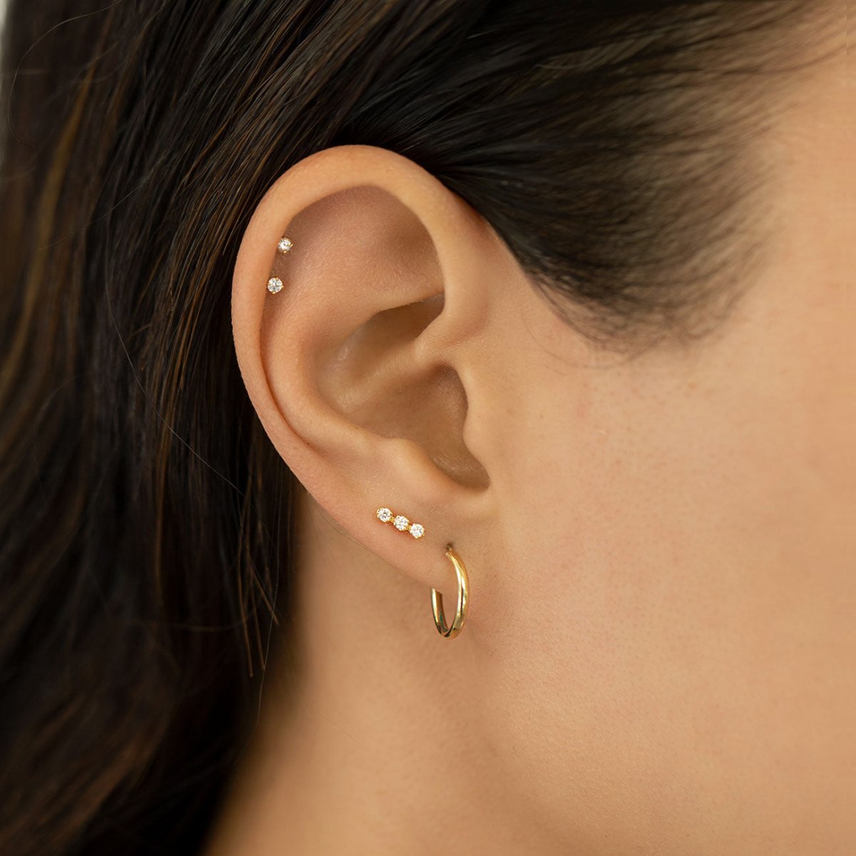 14K gold diamond stud shown on a model's lobe below stacked ear piercings and a plain gold hoop