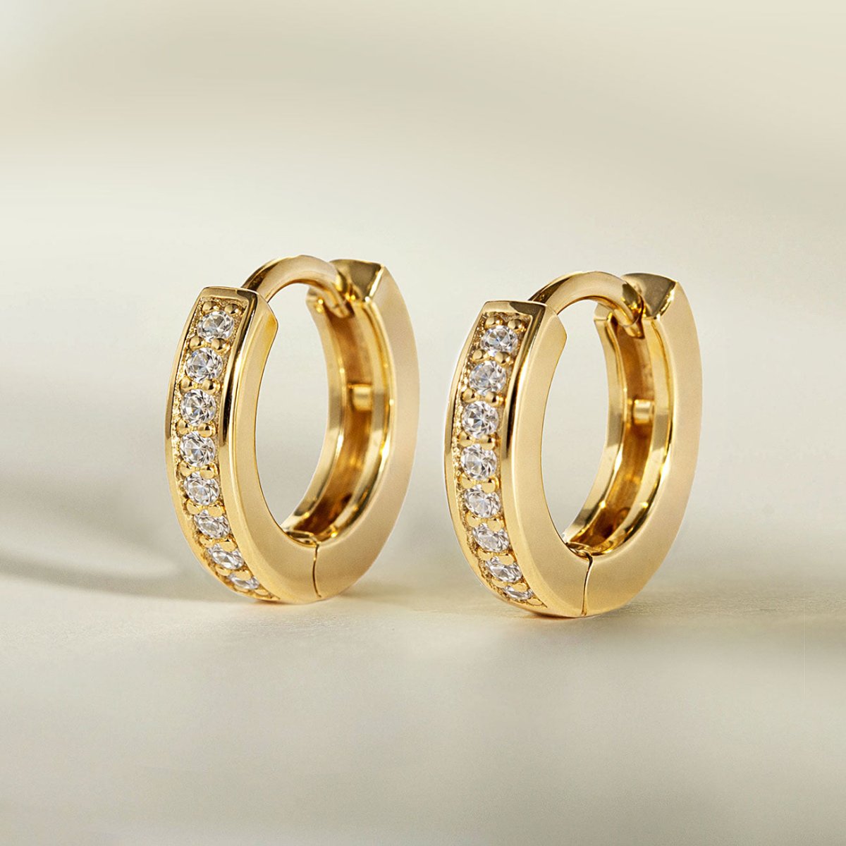 Gold vermeil pave huggie hoops with a row of clear white zirconia, three-quarter view on a cream background