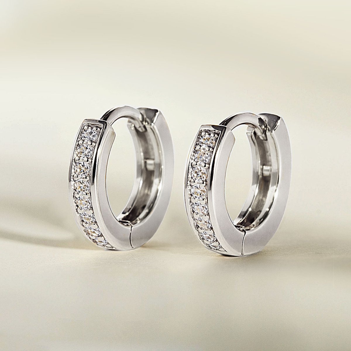 Sterling silver pave huggie hoops with a row of clear white zirconia, three-quarter view on a cream background
