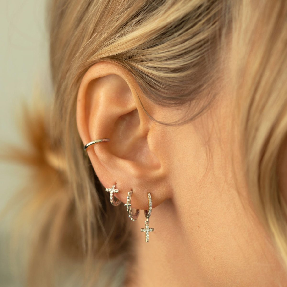 Sterling silver beaded cross huggie hoops styled in an ear stack on a model's ear