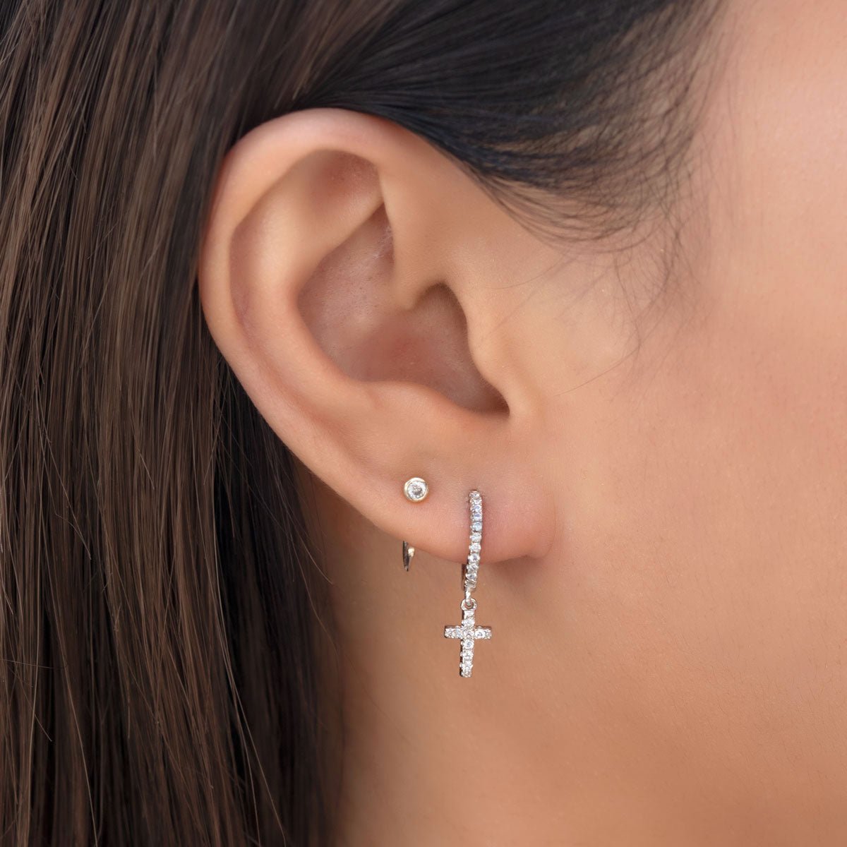Sterling silver pavé huggie hoop with a dangling pavé cross, shown close-up on a model's lobe