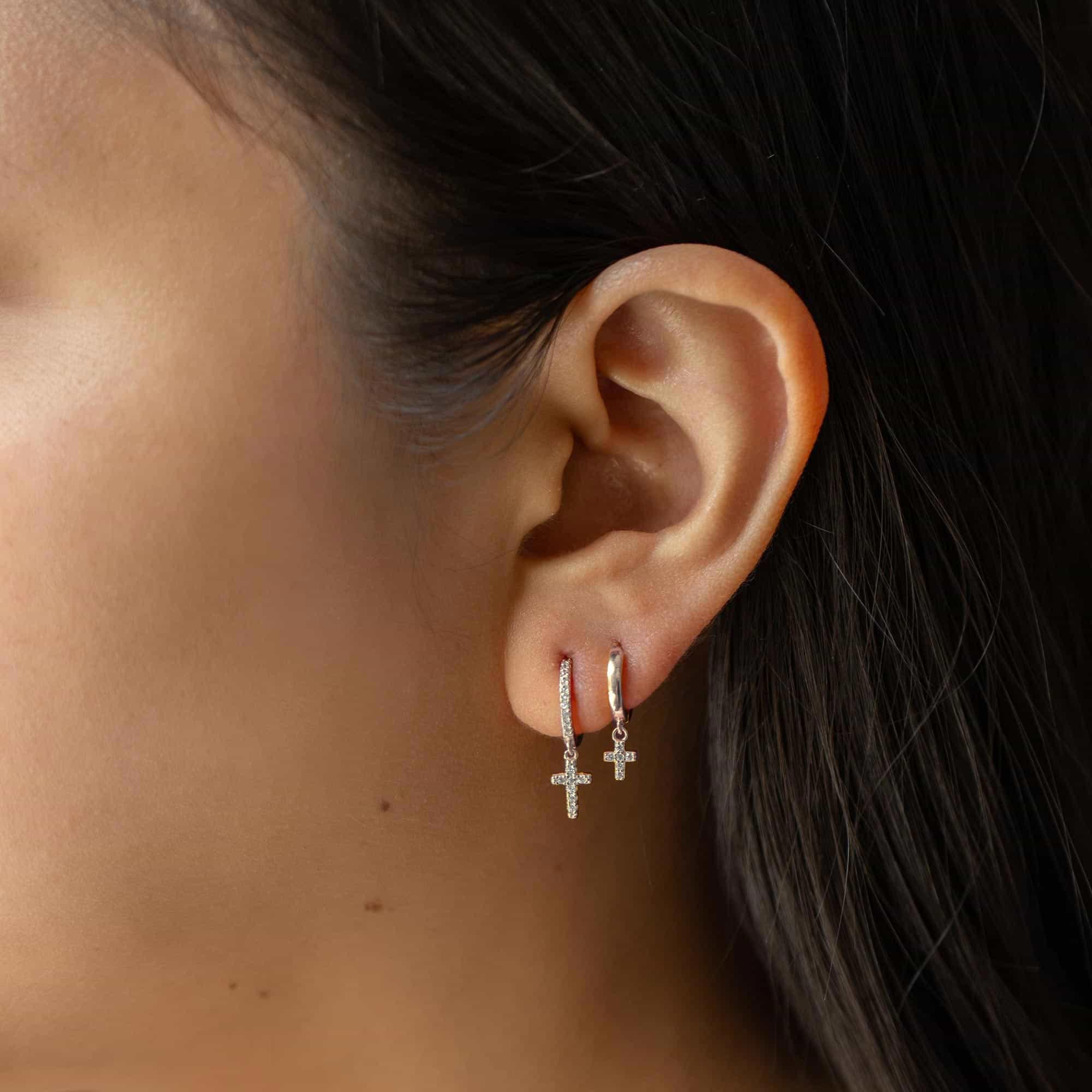 Sterling silver white zirconia cross dangle huggie hoops worn on a model's lobe and second piercing