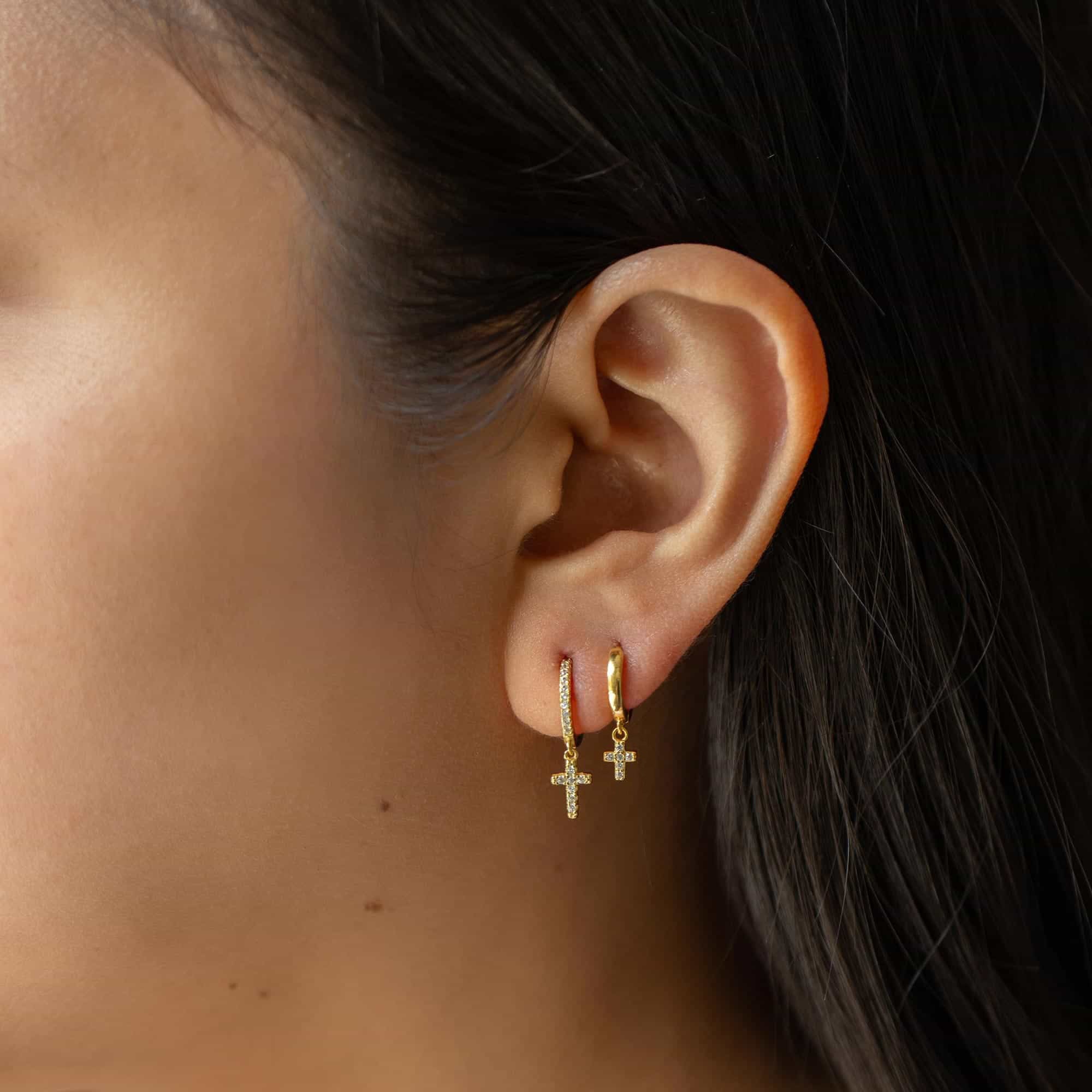 Gold vermeil pavé huggie hoops with dangling pavé cross charms, shown on a model's lobe
