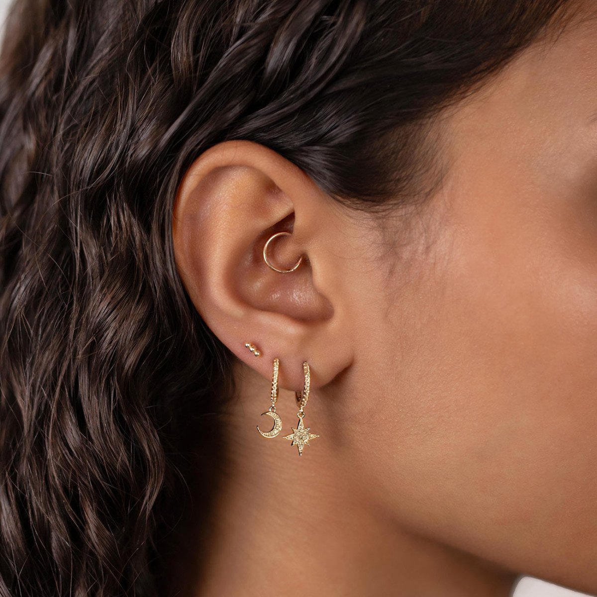 Gold vermeil pavé huggie hoops with star and crescent moon charms, shown on a model's lobe