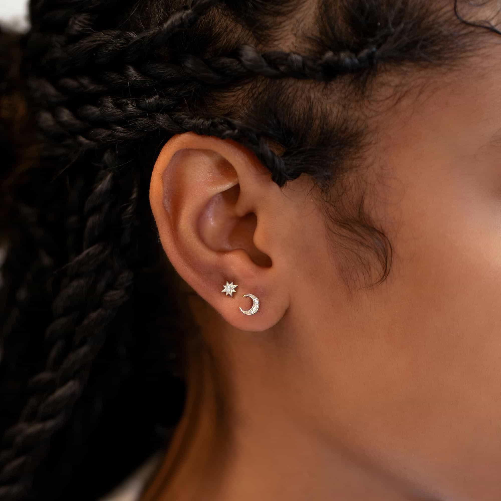 Sterling silver star and crescent moon studs with clear pavé stones, shown close on a model's lobe