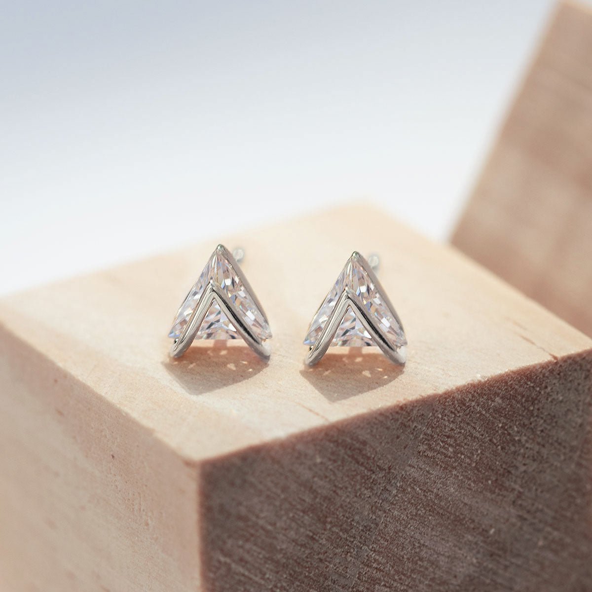 Sterling silver chevron white zirconia studs, close-up detail resting on a wood block