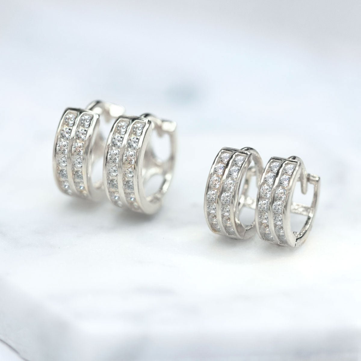 Sterling silver double row pavé huggie hoops with clear stones, close-up detail on white marble
