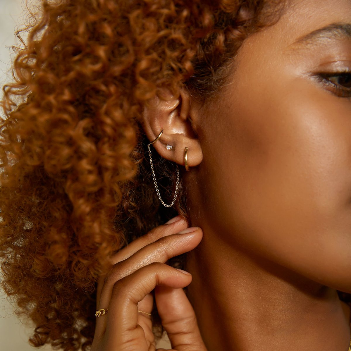 Gold vermeil ear cuff with a draped chain and white zirconia stud, shown on a model's ear