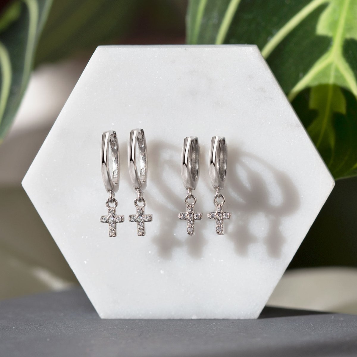 Sterling silver white zirconia cross dangle huggie hoops shown on white marble with greenery