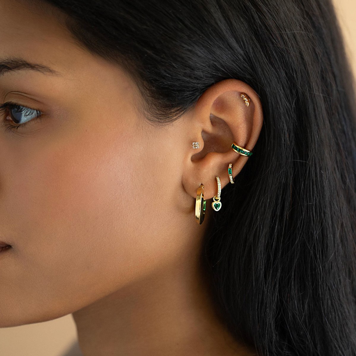 Gold hoops, ear cuff and green-stone earrings styled in an ear stack on a model's ear