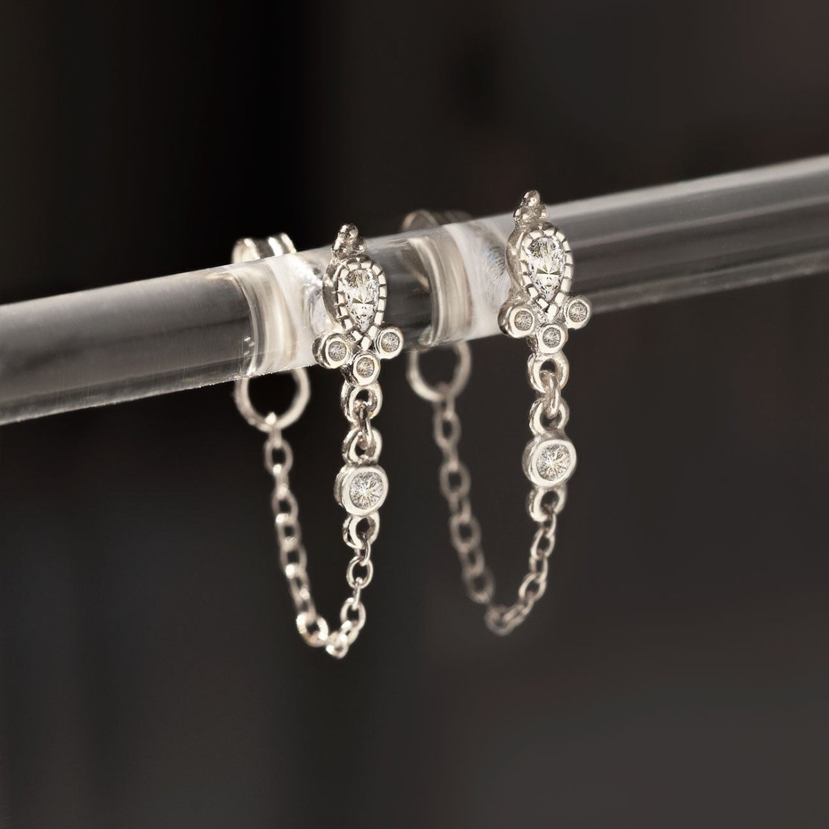 Sterling silver chain-wrap stud earrings with white zirconia, close-up detail on a clear stand