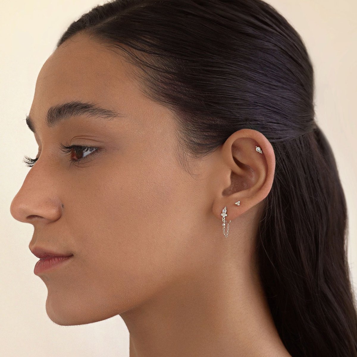 Silver studs with clear stones and a draped chain stud shown on a model's ear