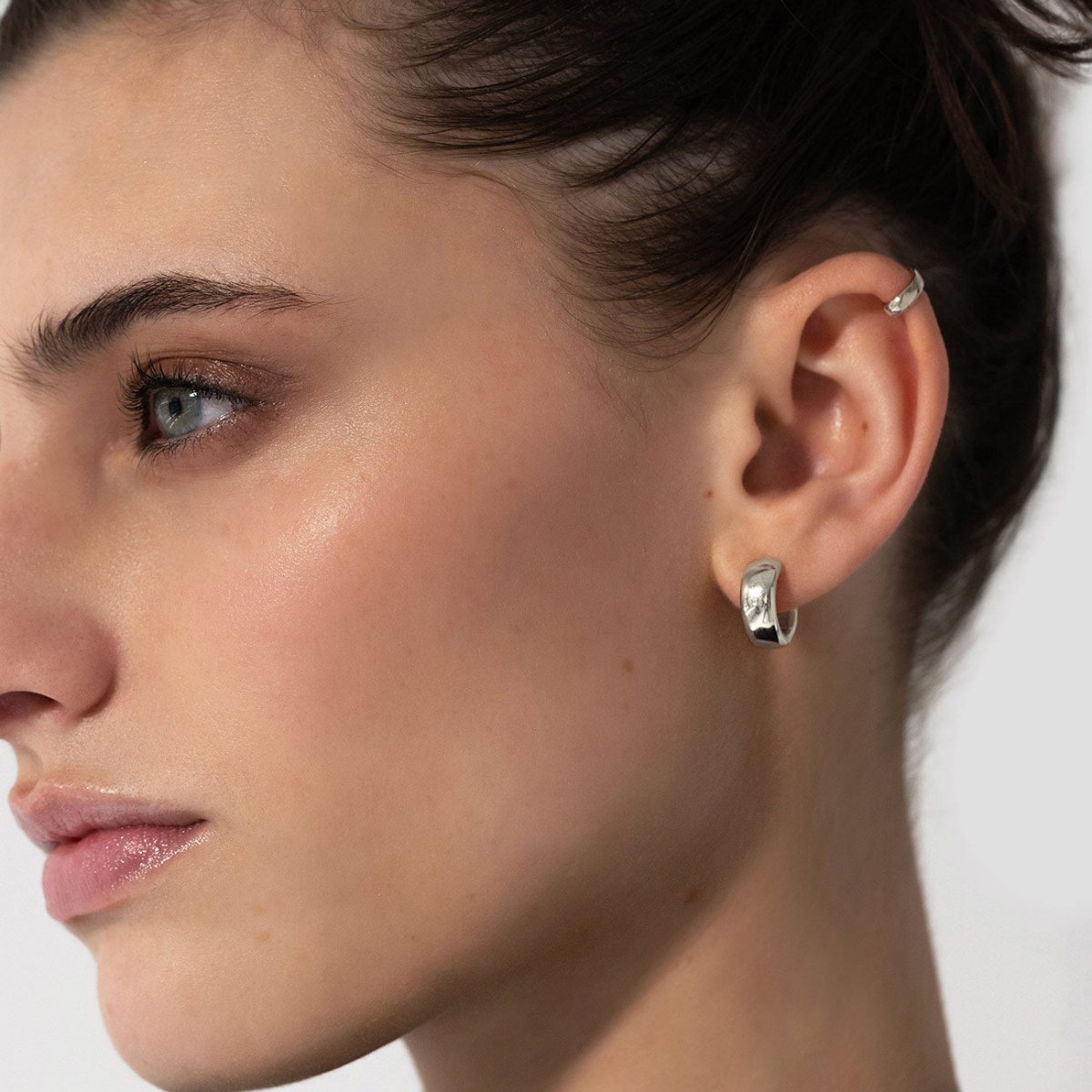Sterling silver chunky mini huggie hoop shown on a model's lobe with a twisted ear cuff above