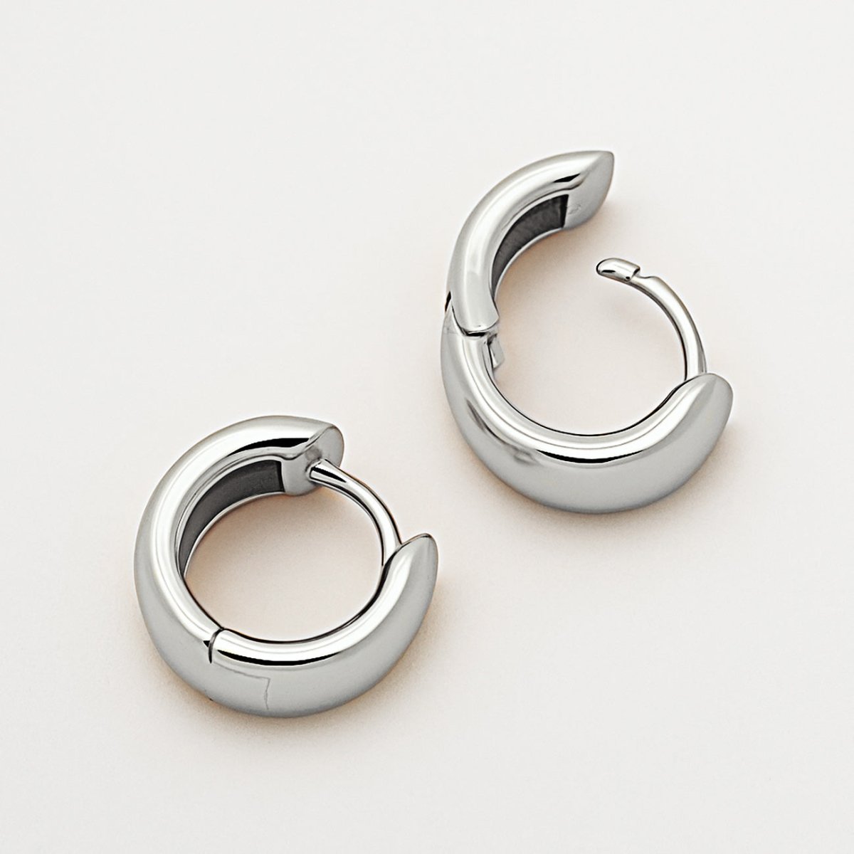 Sterling silver chunky rounded mini huggie hoop earrings with a hinged closure, on a white background