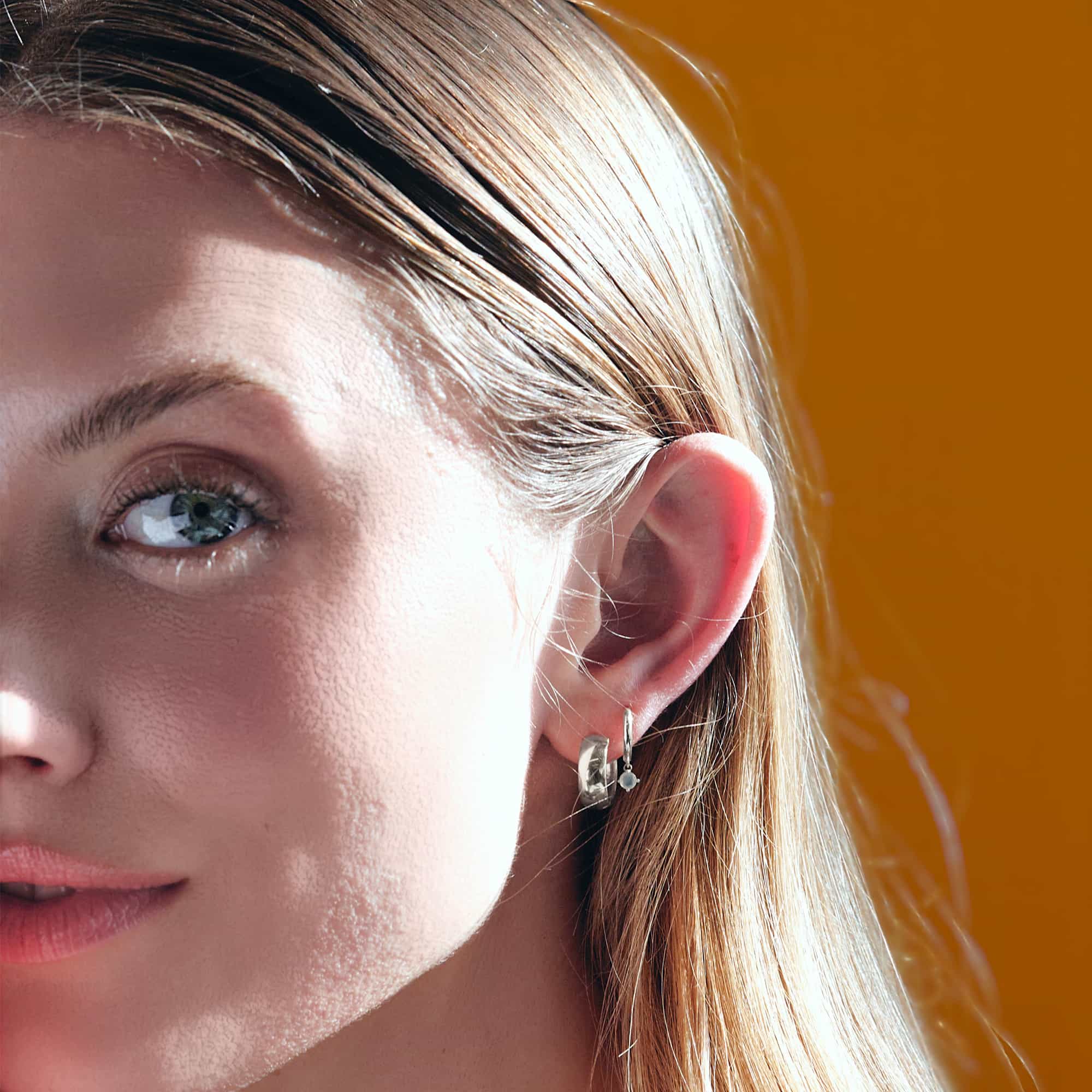 Close-up of woman's ear featuring 14K White Gold Pavé Dangle Huggie Earrings paired with Boyfriend Mini Hoop Earrings 