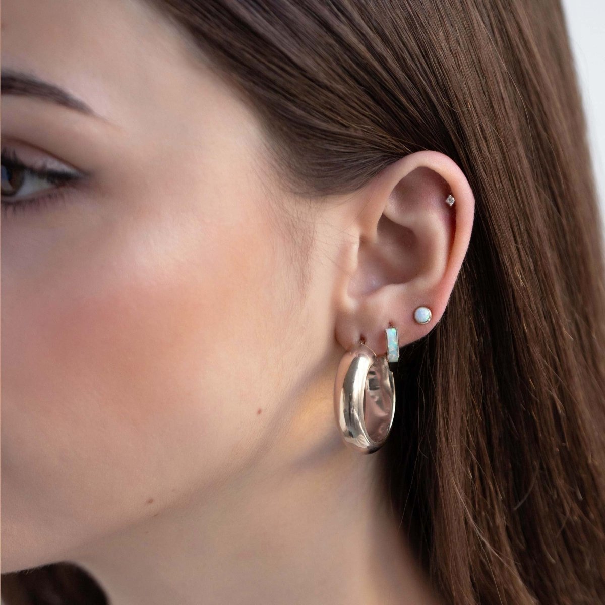 14K white gold white opal huggie hoop shown on a model's lobe with a dome hoop and opal stud