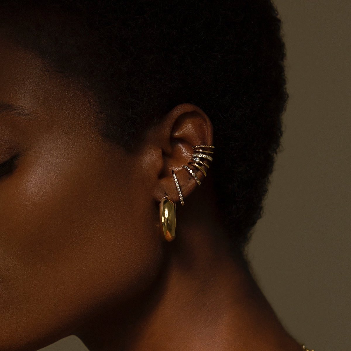 Gold crystal cartilage cuff with a chunky hoop, shown stacked on a model's ear