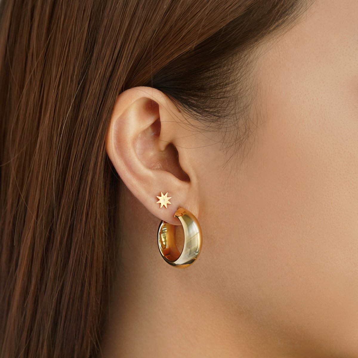 14K gold eight-point starburst stud shown on a model's lobe above a wide gold hoop