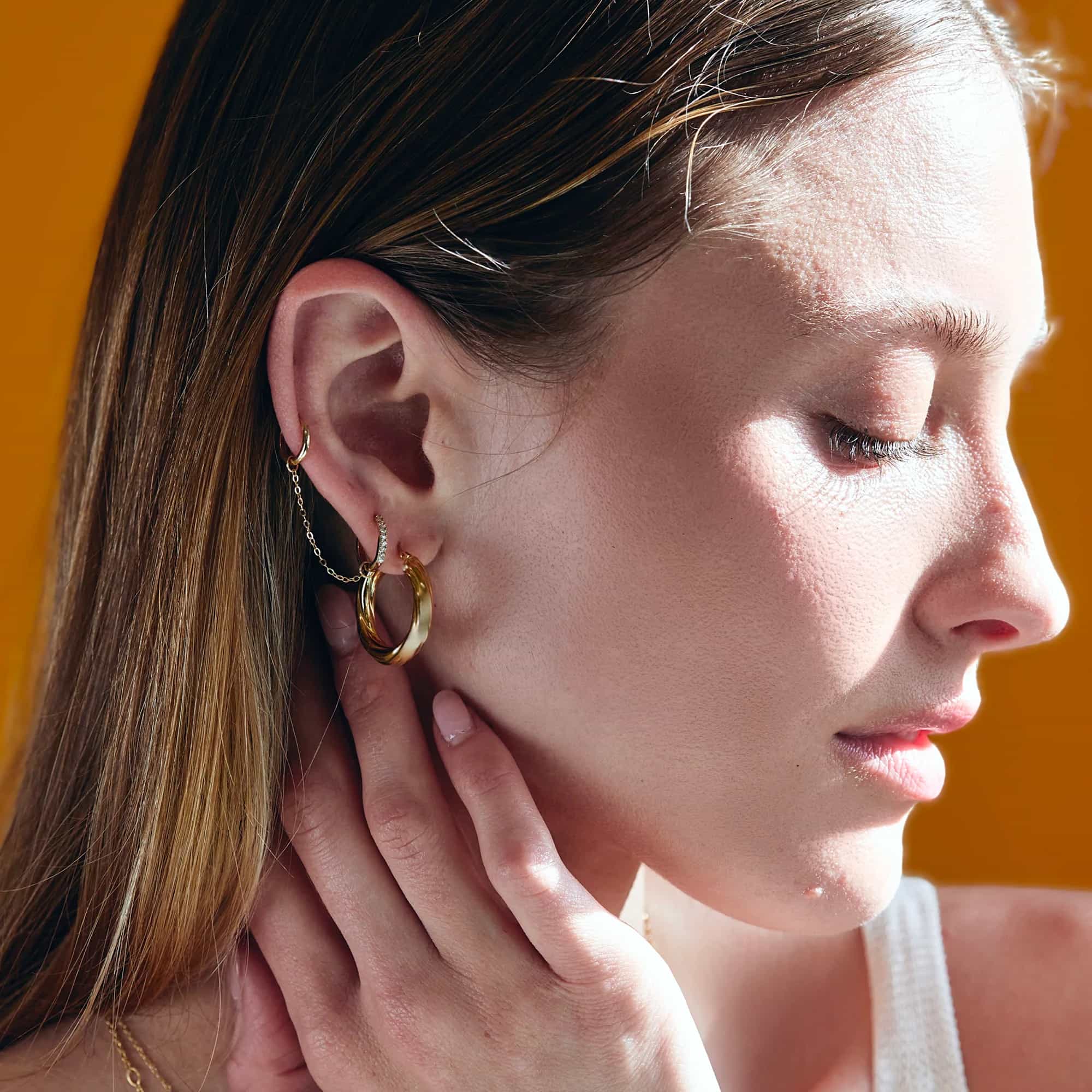 Close-up of woman's side profile featuring 14K Gold Thin Pave Huggie Hoops White Zirconia Crystals and Gold Hoop. 