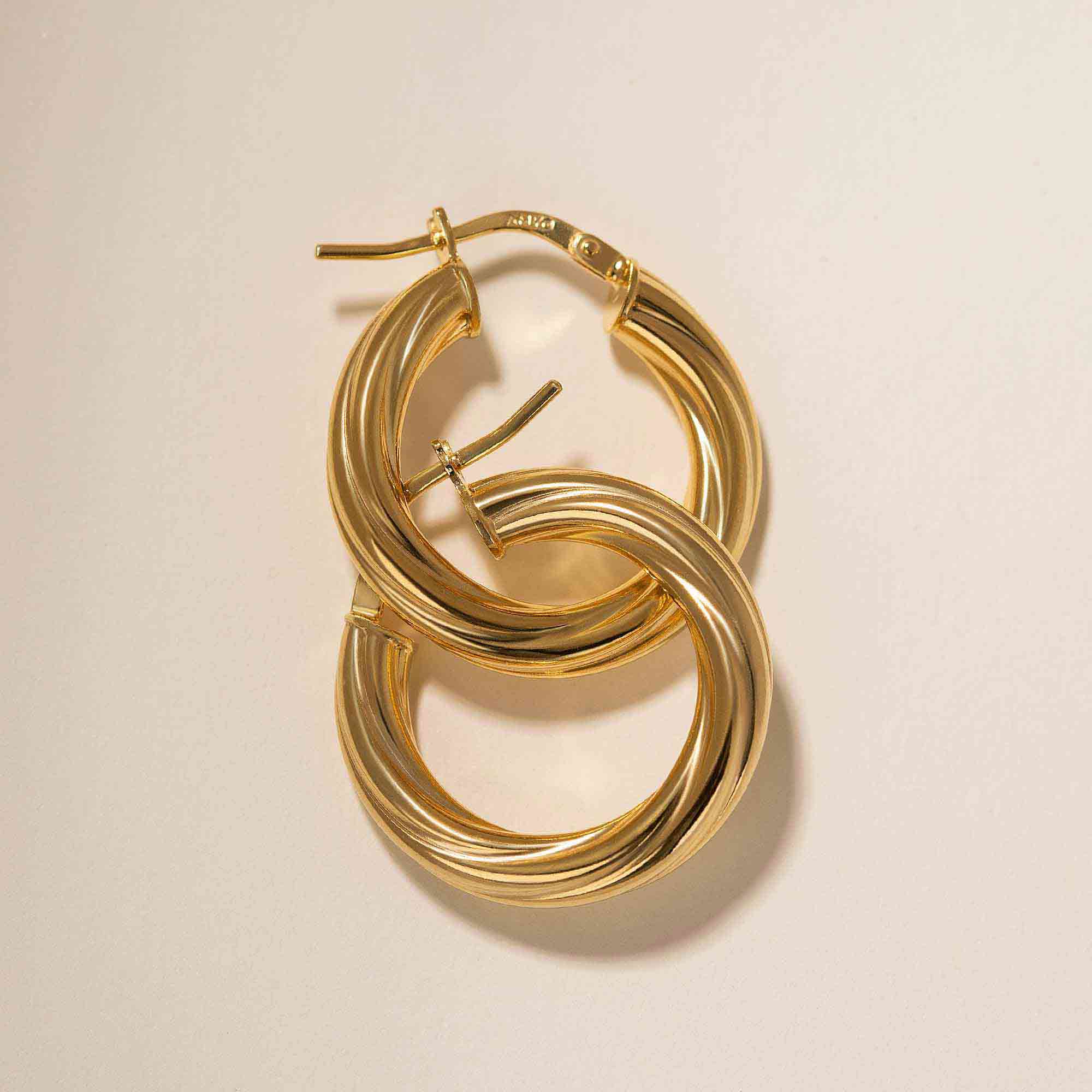 Gold vermeil thick twisted hoop earrings interlinked, close-up detail on a cream background