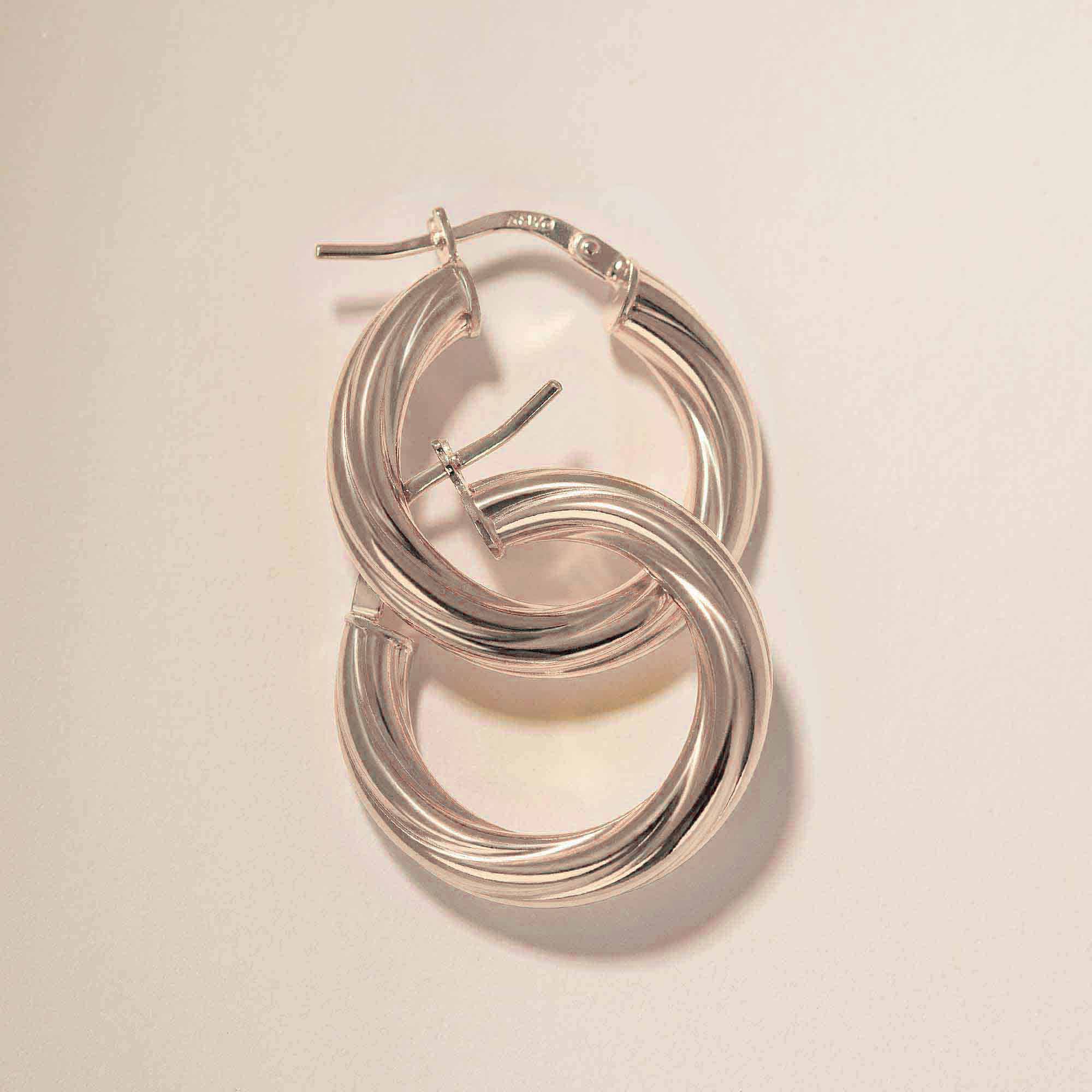 Sterling silver thick twisted hoop earrings interlinked, close-up detail on a cream background