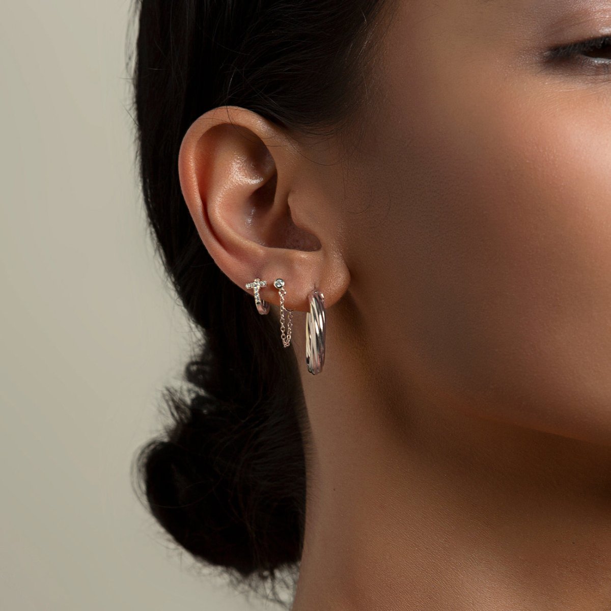 Sterling silver bezel stud with a looping chain shown close-up on a model's lobe