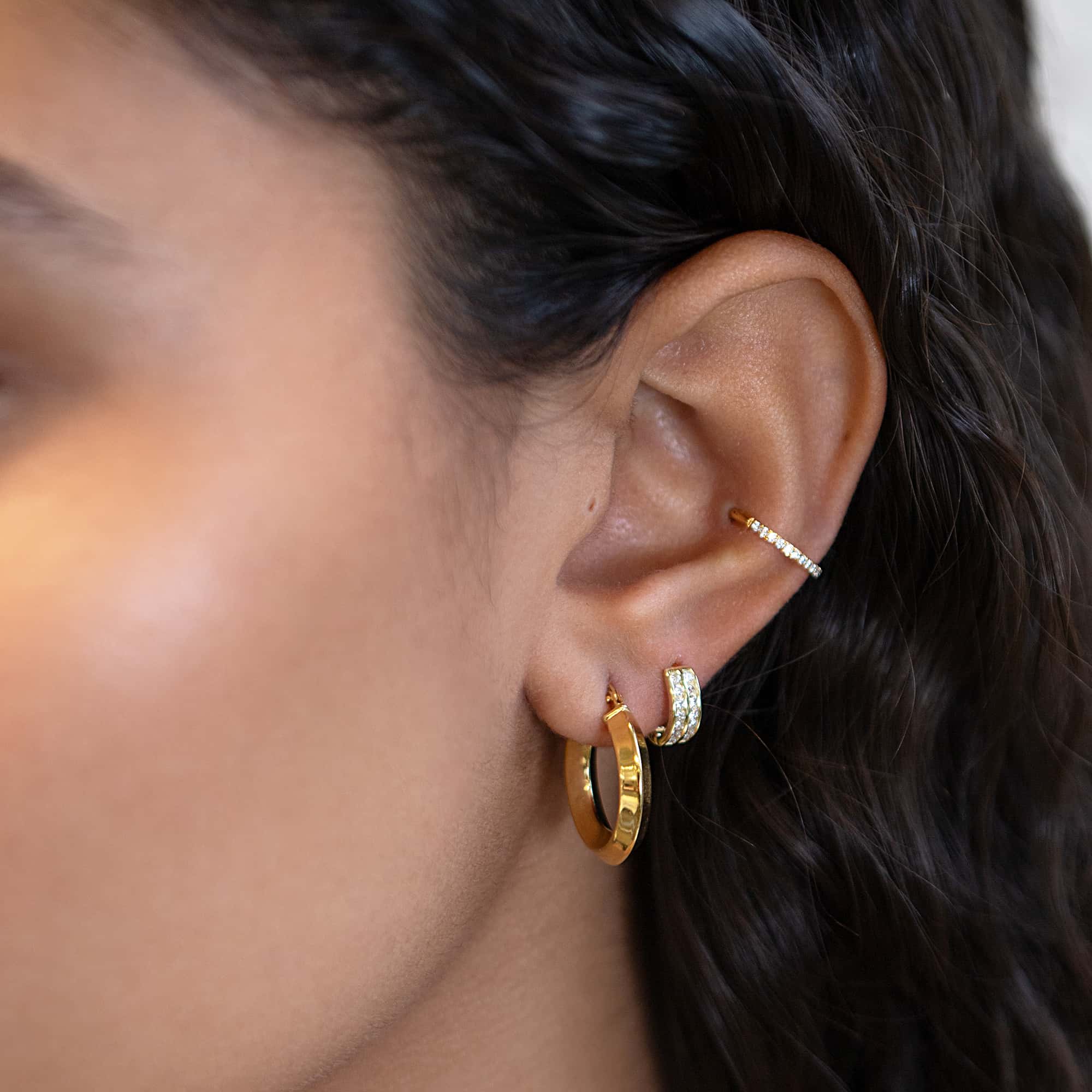 Gold vermeil mini hoop on a model's lobe, stacked with a pavé huggie and pavé ear cuff