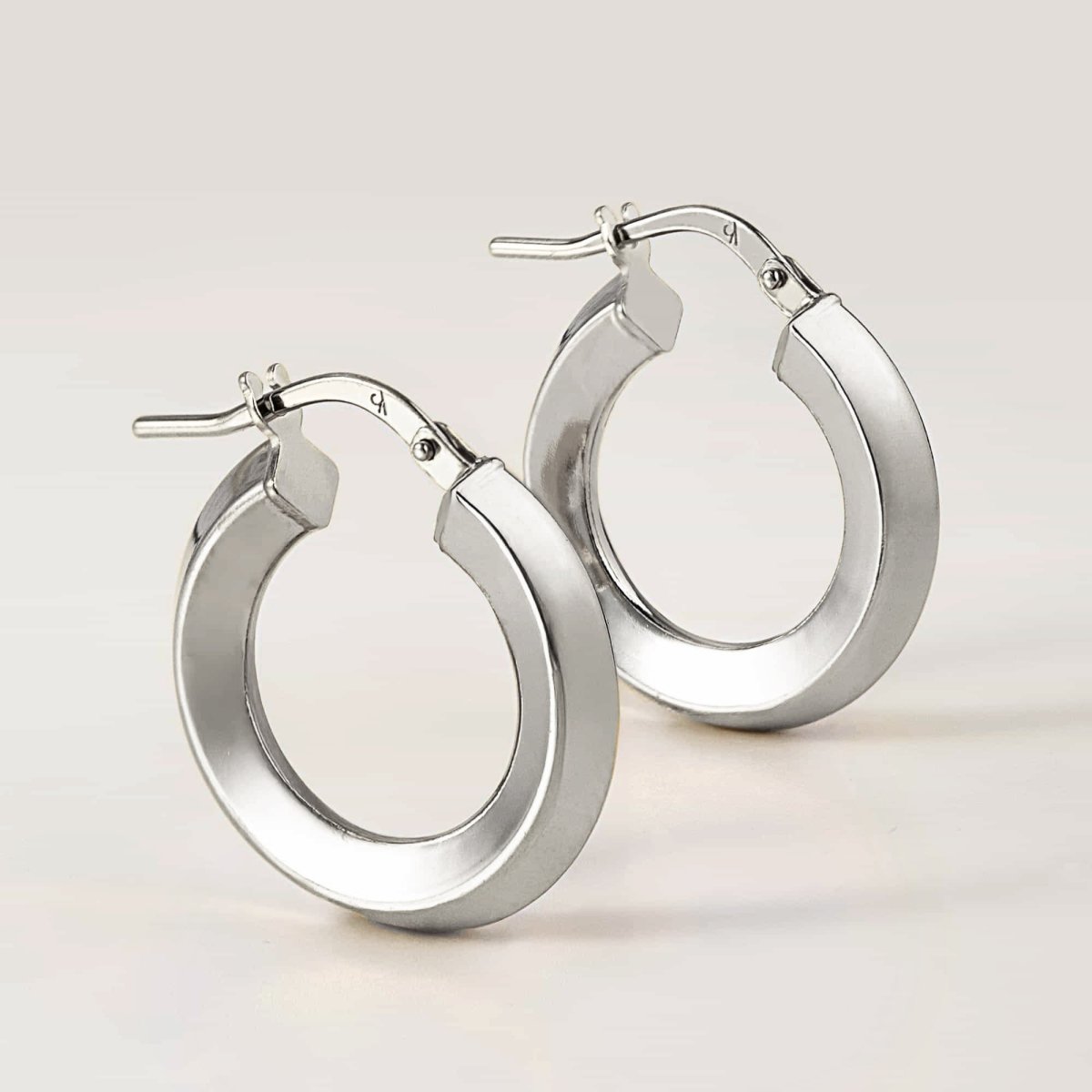 Pair of sterling silver mini hoop earrings with a flat polished edge and hinged closure, on a white background