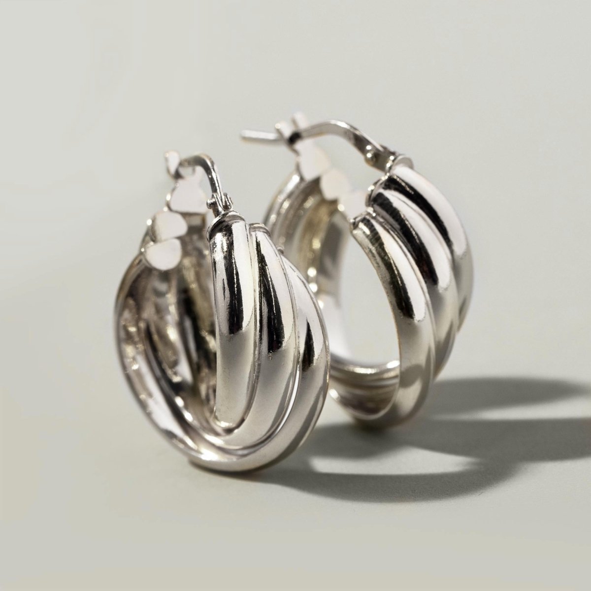 Sterling silver chunky twisted-rope hoop earrings, close-up detail on a cream background