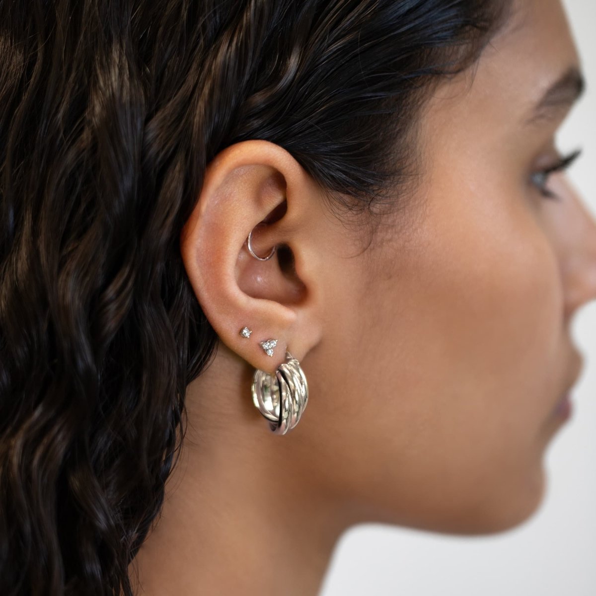 Sterling silver round zirconia trinity cluster stud worn above silver hoops on a model's lobe