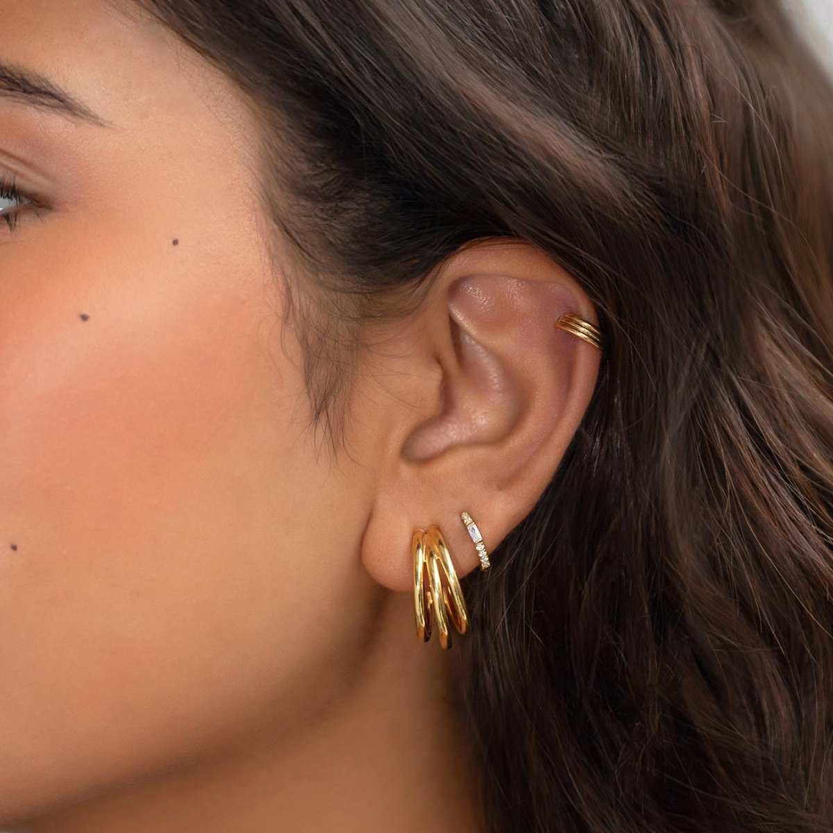 Gold and silver hoops and an ear cuff stacked on a model's lobe and helix