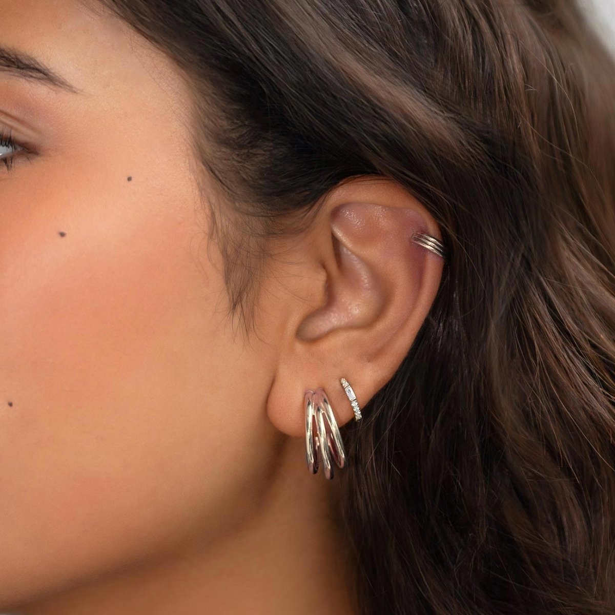 Sterling silver triple hoop earring shown on a model's lobe with a helix ear cuff above