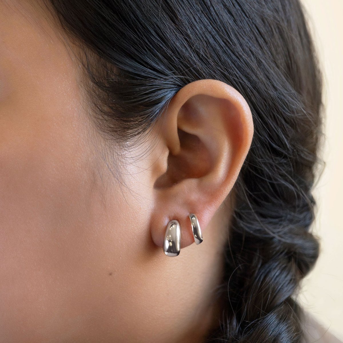 Sterling silver chunky tapered J-hoop earrings shown stacked on a model's lobe and second piercing