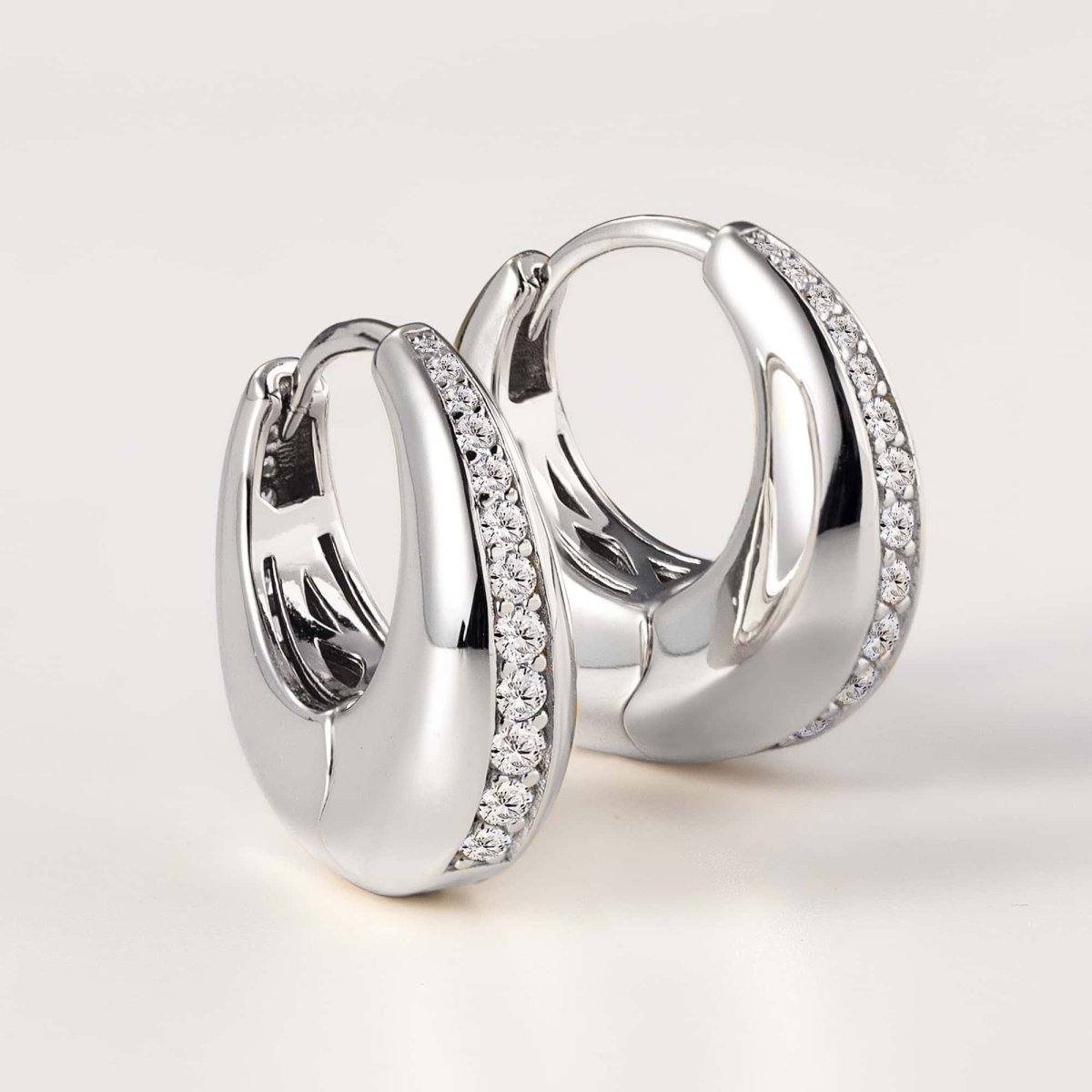Sterling silver chunky huggie hoops with a pavé zirconia inlay, close-up detail on a pale background
