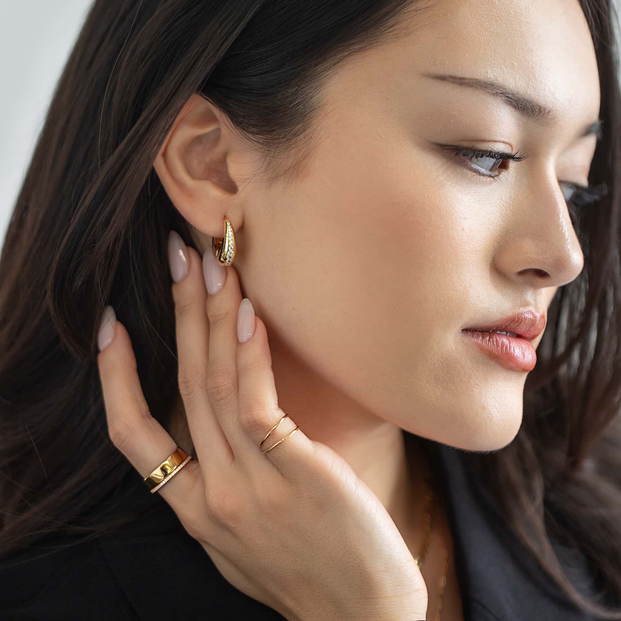 Gold vermeil chunky huggie hoops with a pavé zirconia inlay, shown on a model's lobe with rings on her hand