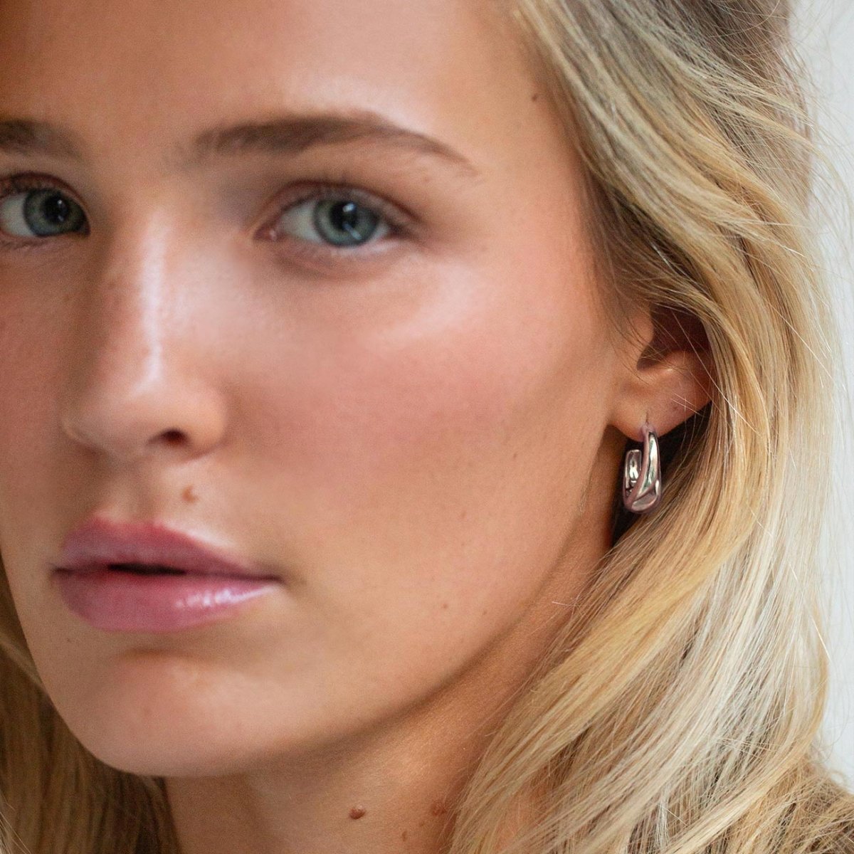 Sterling silver tapered C-shaped huggie hoop shown on a model's lobe