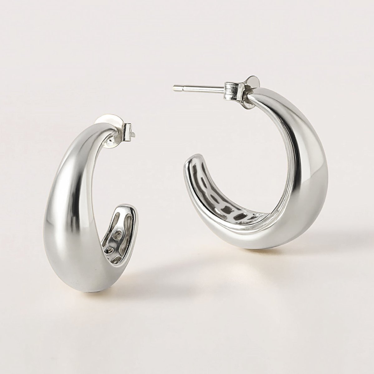 Sterling silver tapered C-shaped hoop earrings, three-quarter view on a cream surface