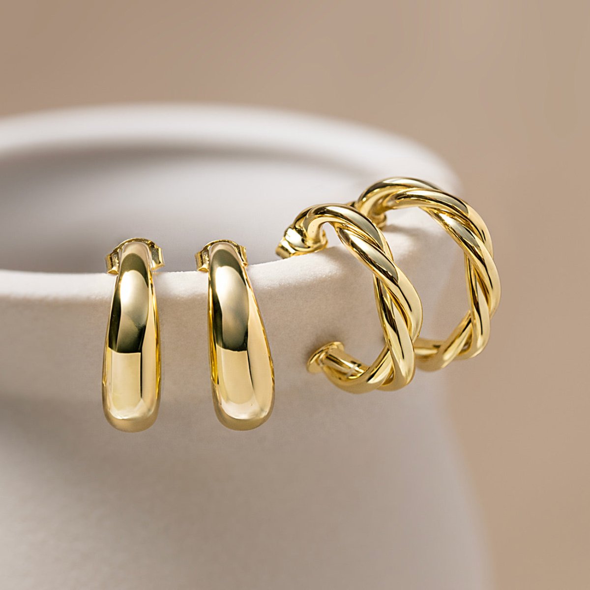 Gold vermeil tapered C huggie hoops beside twisted gold hoops, on a cream background