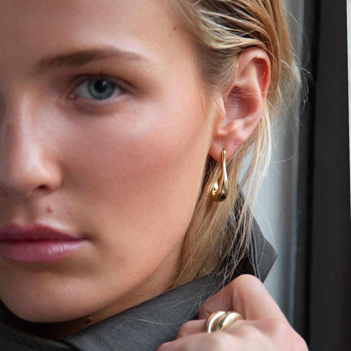 Gold vermeil sculptural J-hoop earring shown on a model's lobe, close-up