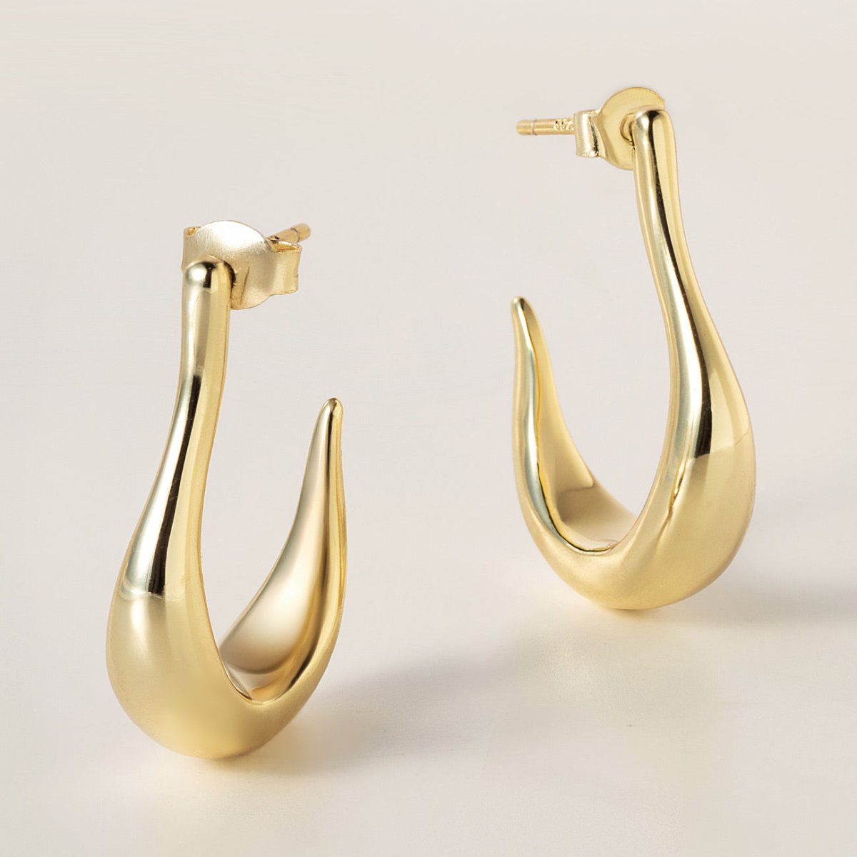 Gold vermeil sculptural J-hoop earrings with post backs, shown on a cream background