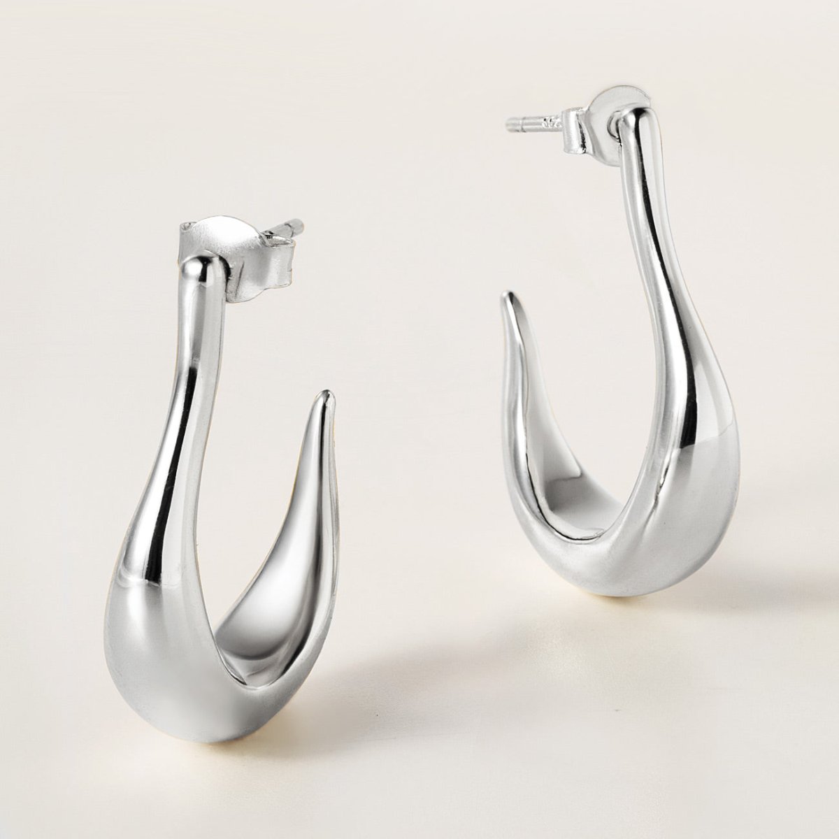 Sterling silver sculptural J-hoop earrings with post backs, shown on a cream background