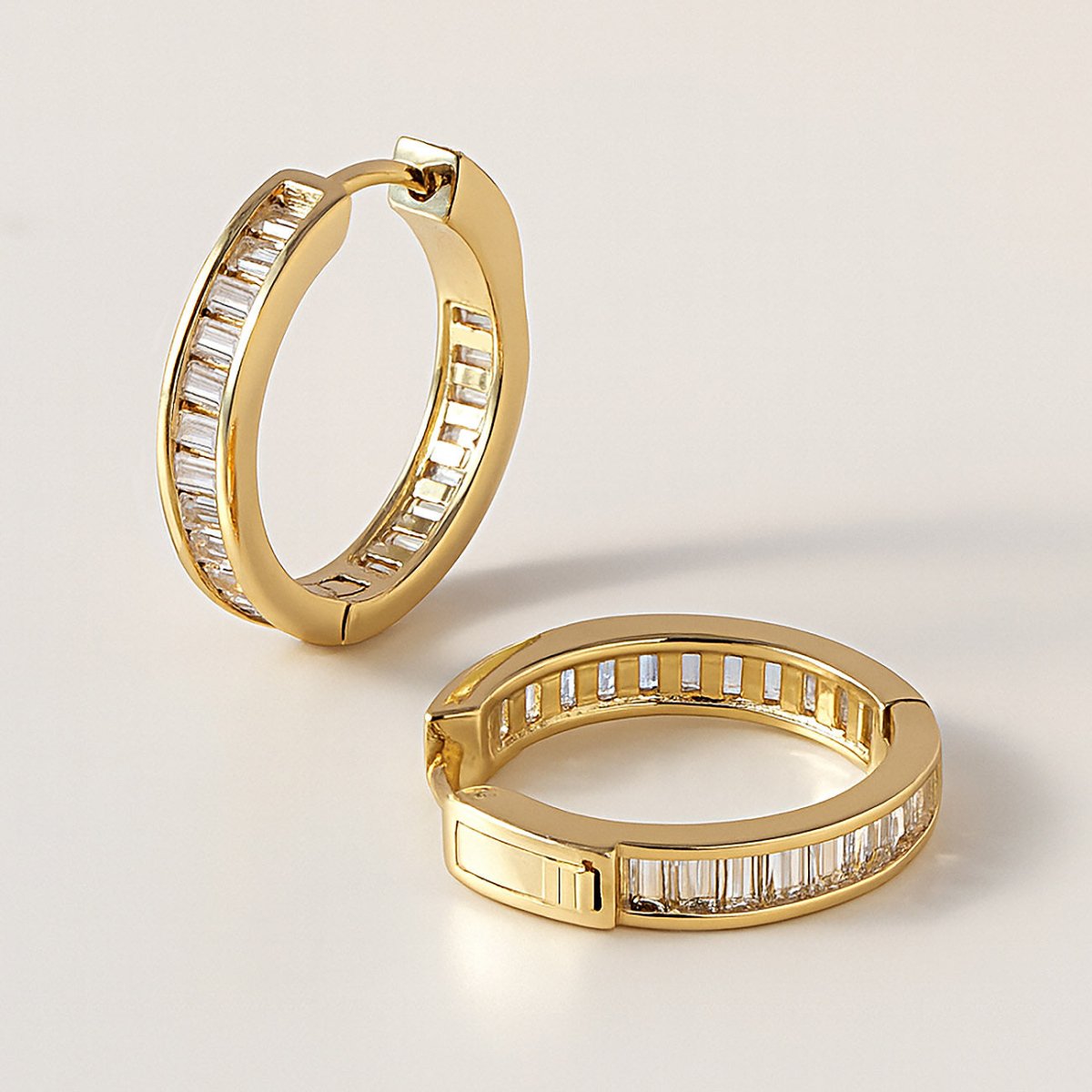 Gold vermeil channel-set baguette huggie hoops with clear stones, pair shown open on a cream background