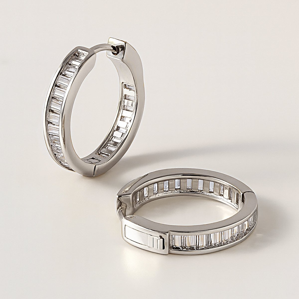 Sterling silver channel-set baguette huggie hoops with white zirconia, pair shown open on a cream background