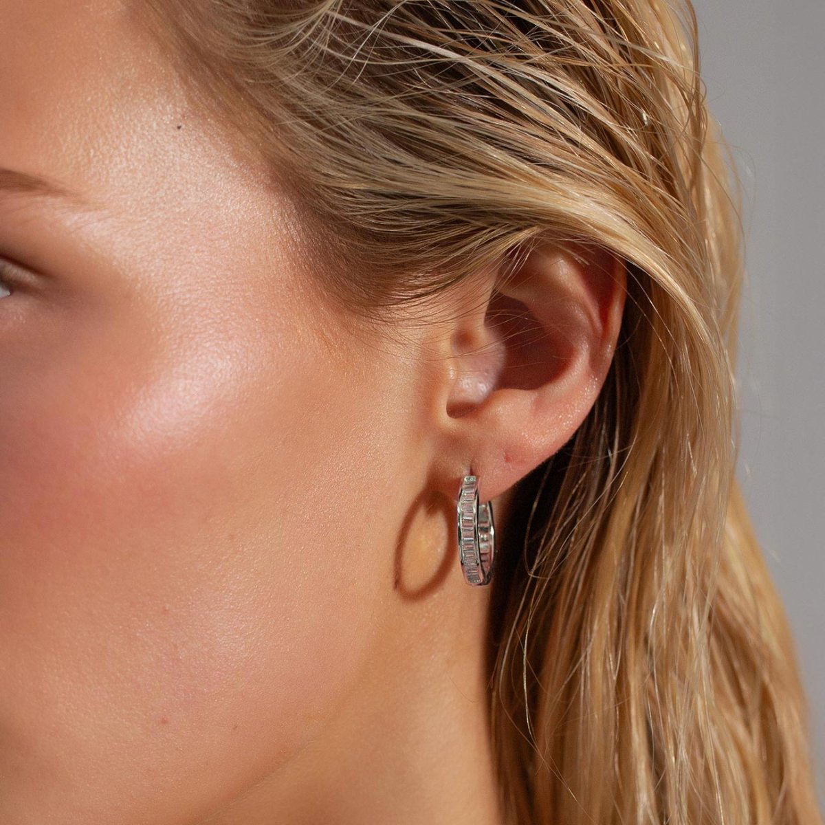 Sterling silver channel-set baguette huggie hoop with white zirconia, shown on a model's lobe