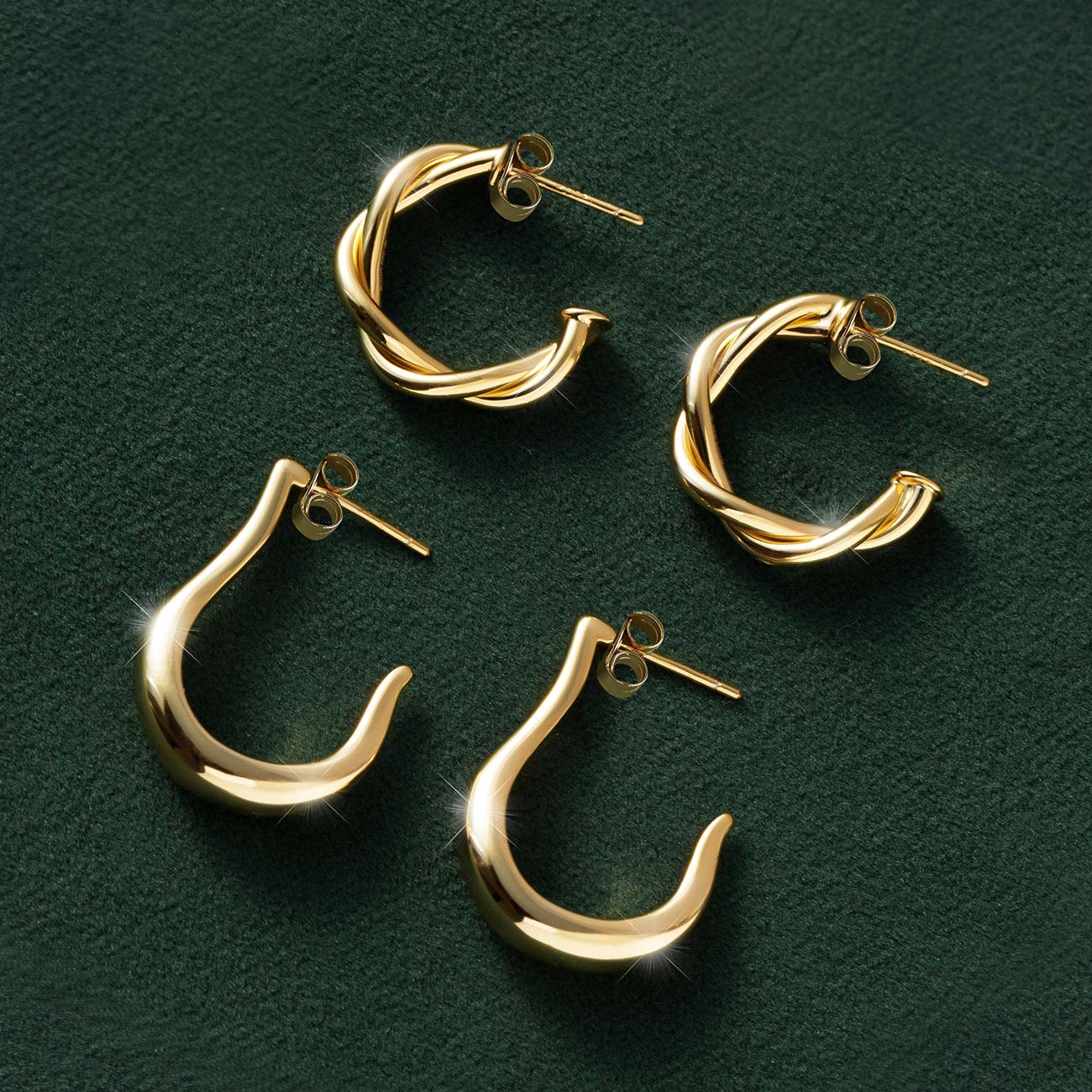 Gold twisted rope and smooth J-hoop earrings in two sizes, laid on dark green velvet