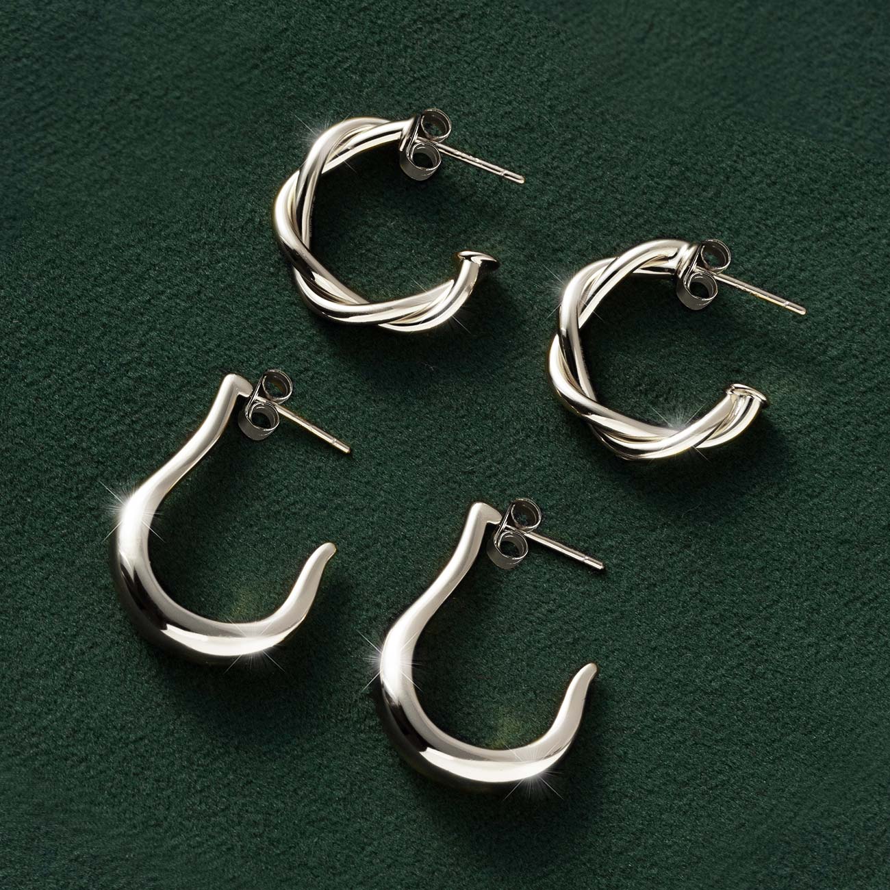 Silver twisted rope and smooth J-hoop earrings in two sizes, laid on dark green velvet