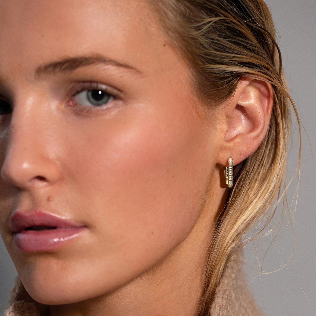 Gold vermeil channel-set baguette oval huggie hoop with clear stones, shown on a model's lobe