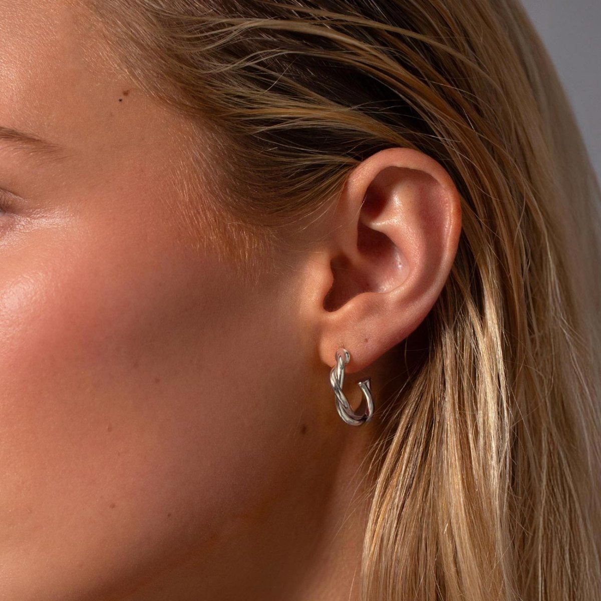 Sterling silver twisted rope C-hoop earring shown close on a model's lobe