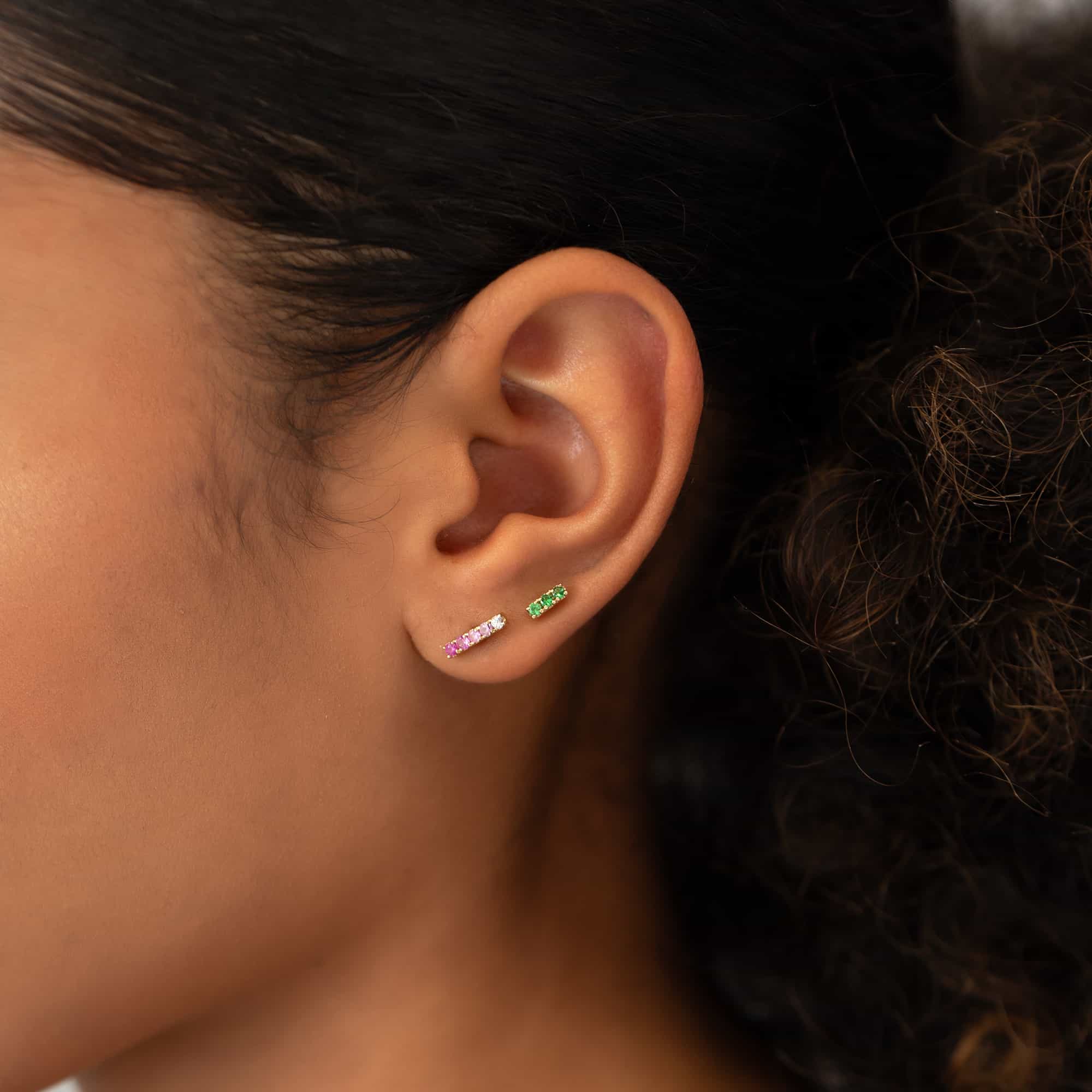 14K gold bar studs with ombre pink sapphire and green stones, shown on a model's lobes