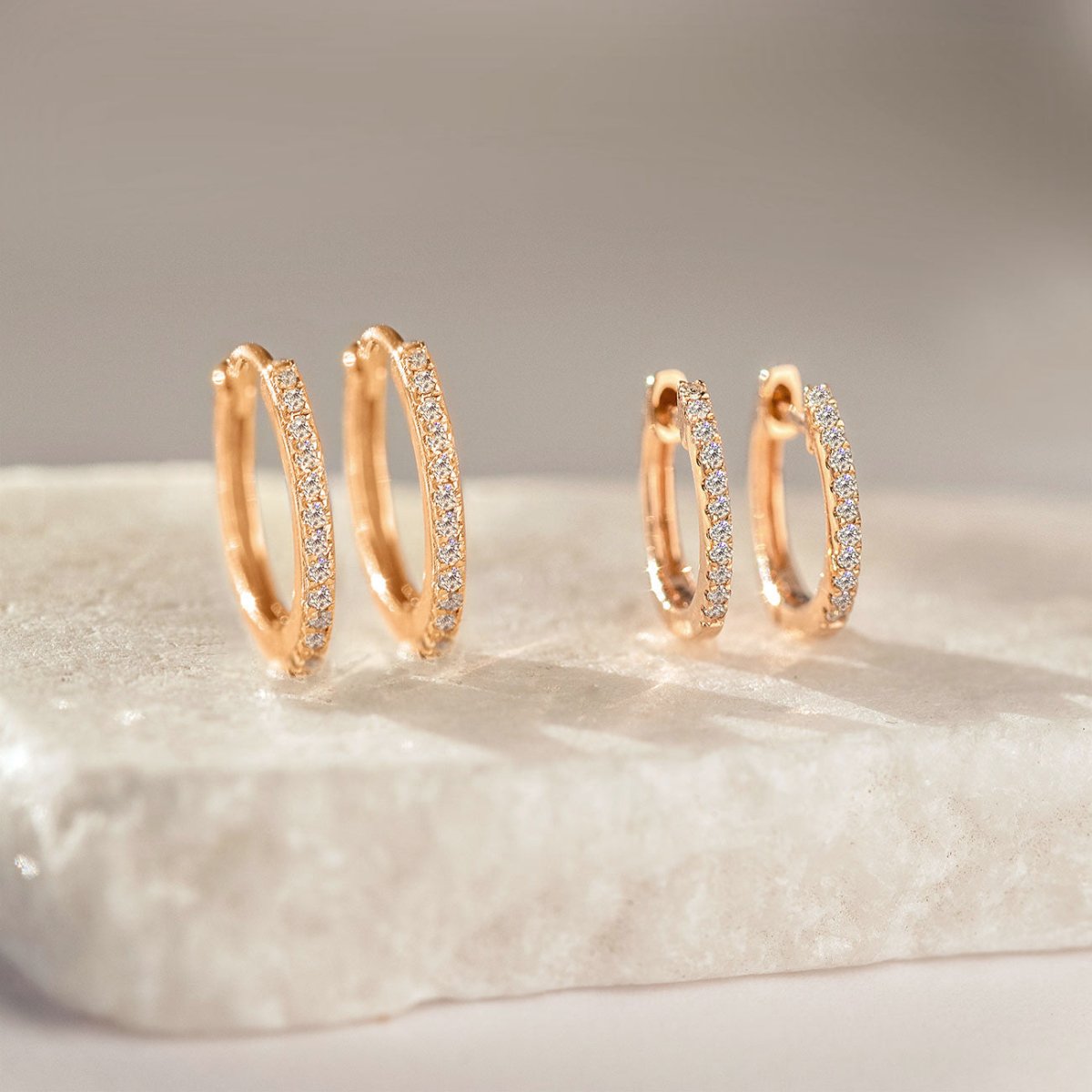 14K rose gold pave diamond huggie hoops in two sizes, on white marble